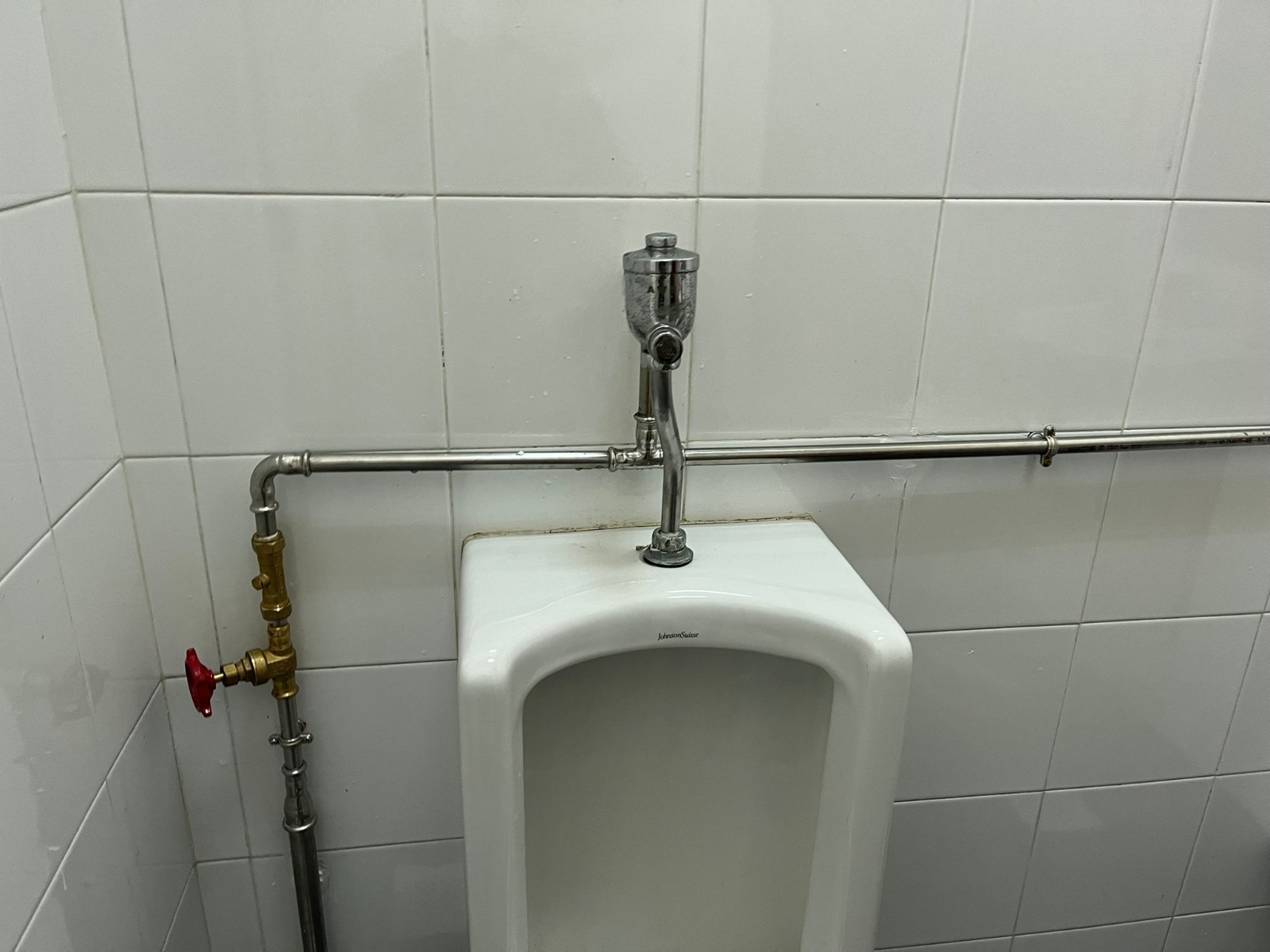 Urinal flush valve and exposed supply pipework with an isolating stopcock in a washroom
