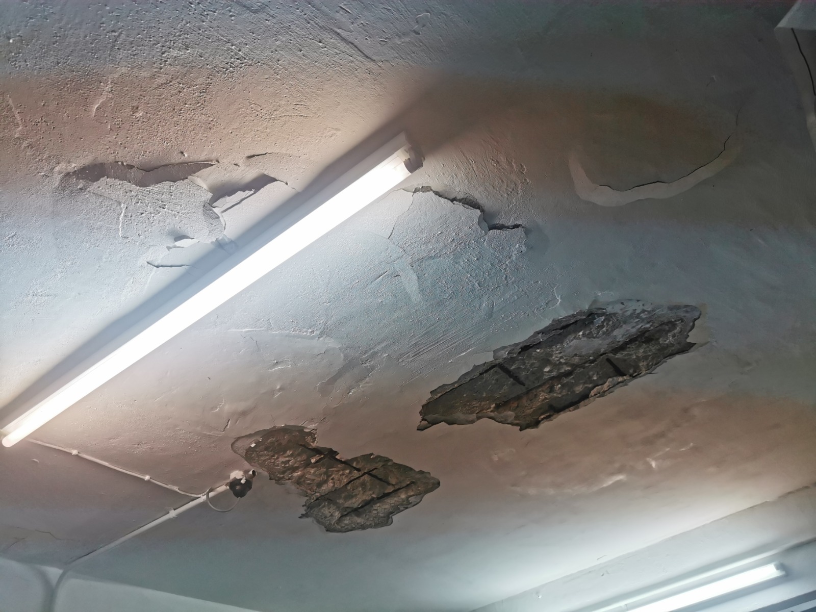 Spalling concrete ceiling with cracked patches and exposed corroded reinforcement bars